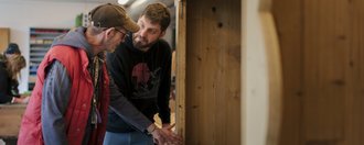Haus Talbach Zwei Menschen stehen in einer Schreinerwerkstatt und begutachten gemeinsam ein Werkstück.